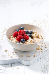 homemade oatmeal with berries on white wooden table, vertical