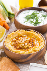 hummus in wooden bowl with pita bread and fresh vegetables, vertical