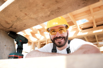 The man is a builder on the roof of a wooden frame house.