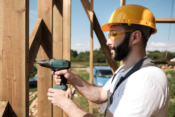 The man is a builder on the roof of a wooden frame house.