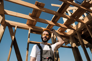 The man is a builder on the roof of a wooden frame house.