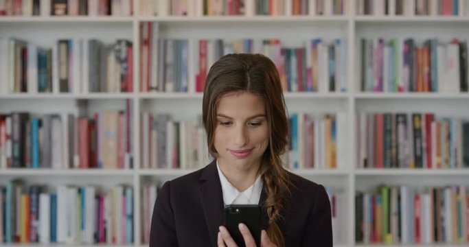 portrait young business woman intern using smartphone browsing sending sms messages enjoying mobile connection in bookstore background independent female entrepreneur