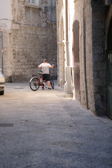 A boy with a bicycle on a narrow street of an ancient city. Italy