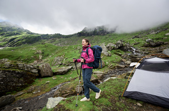 Happy young woman smiling looking around standing near her tent in the mountains while hiking copyspace backpacking trekking equipment lifestyle activity hobby leisure travelling nature.