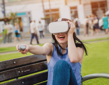 A beautiful young girl plays a game wearing virtual reality glasses on the street.