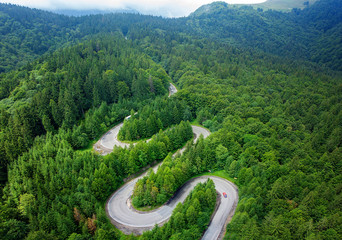 Curved winding road trough the forest aerial view. High mountain pass in Transylvania, Romania....