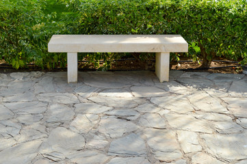 A stone white bench without a backrest in the park for rest on a stone semi-road against the...