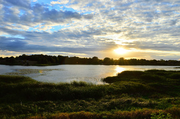 Fototapeta na wymiar Rzeka wśród zieleni i zachodzące słońce.