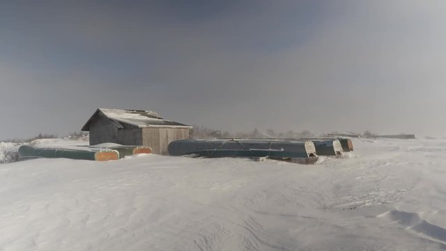 Grounded freighter canoes and boathouse in windy winter snow,  northern Quebec on James Bay