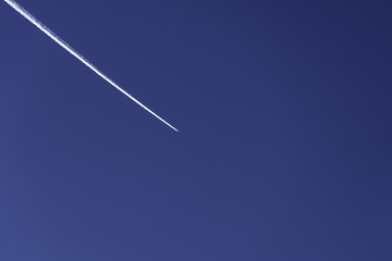 White plane trail in deep blue sky