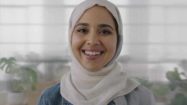 close up portrait of young muslim business woman looking at camera smiling confident wearing traditional hijab headscarf in office workspace background