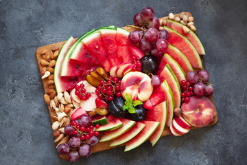 Fruit salad with watermelon, plum, peach, red currant, grape and nuts on wooden tray over dark slate background
