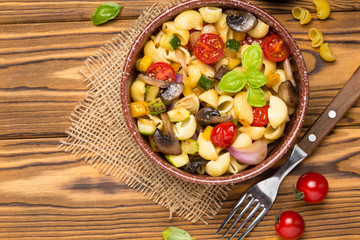 Italian pasta with fried vegetables and mushrooms, zucchini, cherry tomatoes, champignon, cheese and Basil. In dark bowl on wooden background
