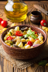 Italian pasta with fried vegetables and mushrooms, zucchini, cherry tomatoes, champignon, cheese and Basil. In dark bowl on wooden background
