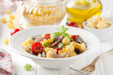 Italian pasta with fried vegetables and mushrooms, zucchini, cherry tomatoes, champignon, cheese and Basil. White plate