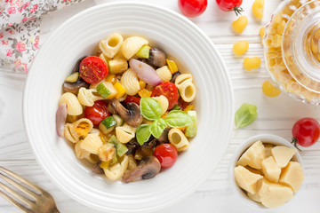 Italian pasta with fried vegetables and mushrooms, zucchini, cherry tomatoes, champignon, cheese and Basil. White plate