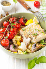 Baked vegetables with mushrooms and white fish fillets in bowl. Zucchini, cherry tomatoes on a branch, red onions, bell peppers and garlic. Healthy diet food