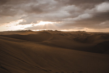 Fototapeta na wymiar Sand dunes of the desert in Huacachina, near Ica, Peru at a cloudy sunset