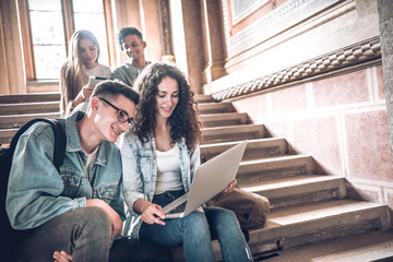 College life.Group of students using a laptop while sitting on stairs in university.