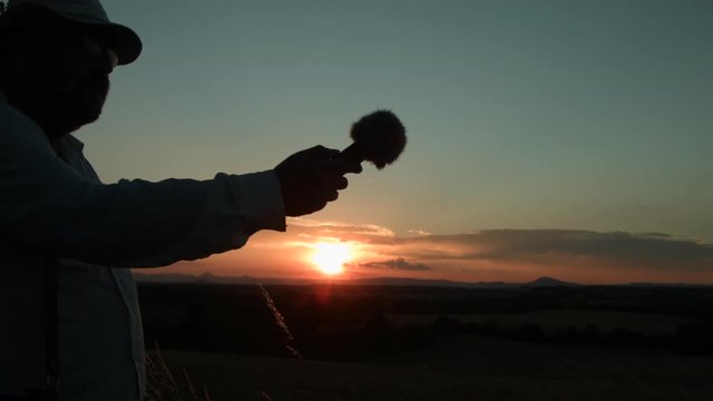 The silhouette of a man who is recording the sound of nature.