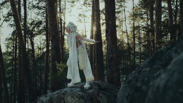 Talented young woman posing on the rock dressed as wood spirit. Model is standing on the giant rock in forest and screaming. Angry satyress.