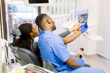 Male african dentist speaking with patient in dental clinic.