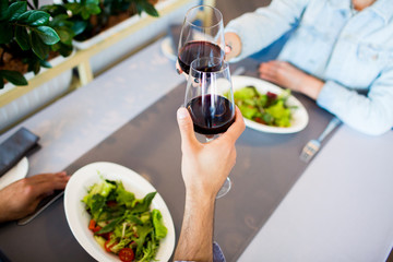 Human hands holding glasses of red wine during toast over served table with plates of salad