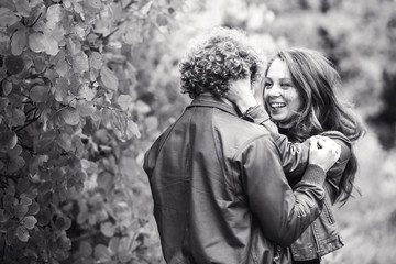 Curly-haired mustachioed man and brown-haired woman hugging in autumn.