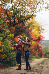 merry couple shows emotions. man and woman in leather jackets and jeans against background of autumn trees. girl closes guy's eyes.