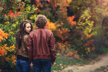 Fototapeta premium curly-haired man turned his back, and girl peeks out from behind his shoulder. loving couple on background of beautiful colorful autumn trees.