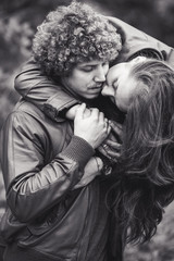 Curly-haired mustachioed man and brown-haired woman hugging in autumn.