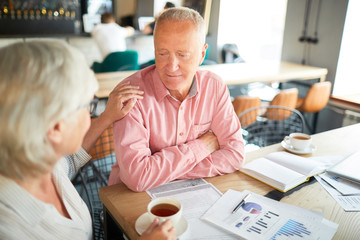 Female colleague supporting mature businessman during working meeting in cafe