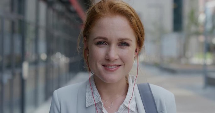 portrait attractive young red head business woman smiling wearing earphones enjoying listening to music in urban city slow motion