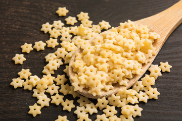 Dry raw star pasta with spoon on wooden table