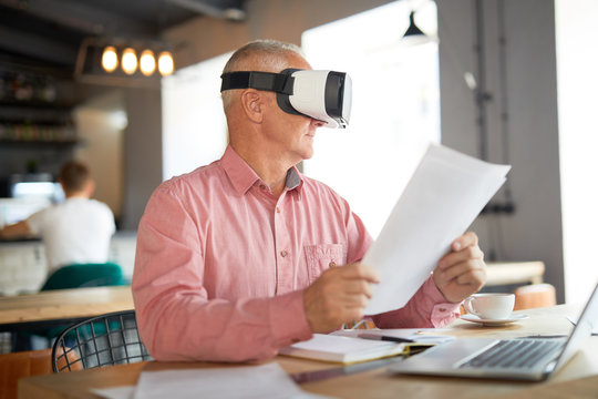 Senior businessman with papers watching virtual presentation or webcast in vr headset