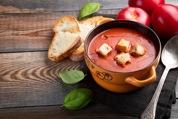 Homemade tomato soup with Basil, toast and olive oil on a wooden table. Prepared a vegetarian dish on a dark background. with copy space