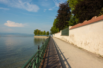 Fototapeta na wymiar Footpath with old iron railing along the castle wall in the park at Lake Constance in Friedrichshafen