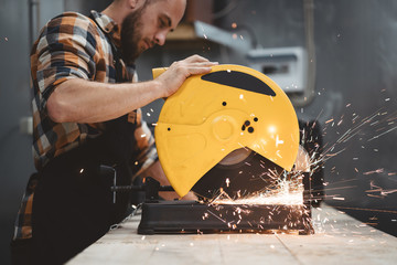 Strong bearded mechanic working on angular grinding machine in metalworking. Work in action. Sparks...