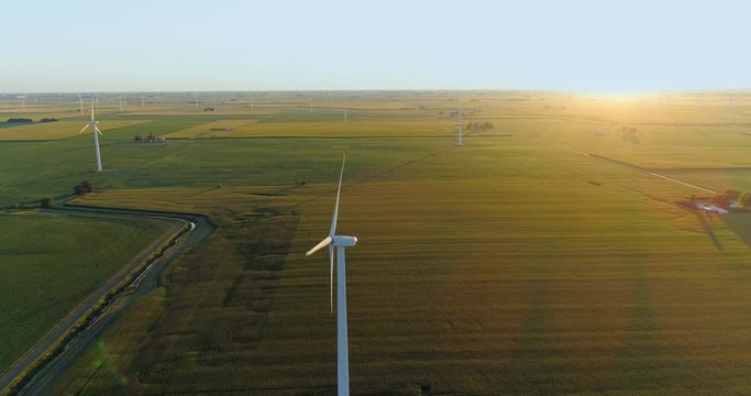 Flying above countryside field and wind farm into sunset with light beams