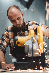 Bearded worker mechanic using electrical angular grinding machine in metalworking. Work in action. Sparks fly apart. Vertical