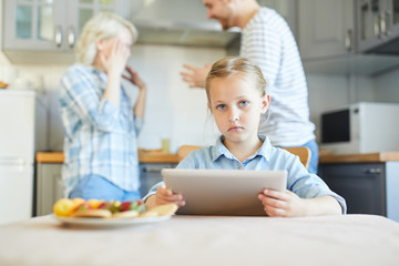 Obraz premium Unhappy little girl with touchpad looking at camera while her parents having argument