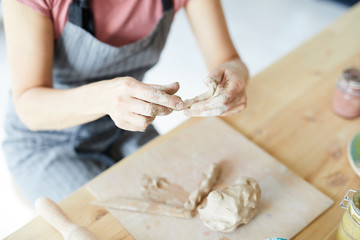 Female hands kneading clay over wooden board with another workpiece for earthenware