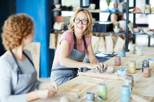Laughing woman talking to colleague during process of making earthenware in workshop