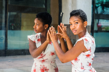 Young African American Woman with short afro hairstyle, standing by mirror in New York, hands touching reflections, head turning around, thinking. Concept of self assured, self esteem, self checking.