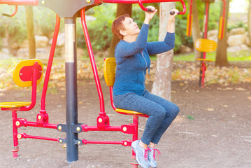 Senior 60-70  year old age woman working out on the sports public equipment in the outdoor gym.A sportive active elderly woman doing physical exercise in a park at sunny day..