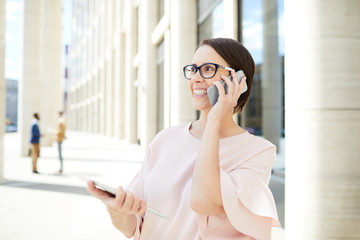 Fototapeta premium Happy businesswoman with smartphone consulting her clients outdoors with colleagues on background