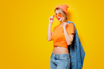 Young style girl with orange glasses on yellow background. Clothes in 1980s style