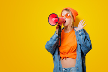 Young style girl in jeans clothes with pink megaphone on yellow background. Symbolizes female...
