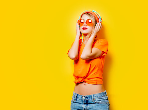 Young style girl with orange glasses and headphones on yellow background. Clothes in 1980s style