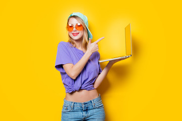 Young style girl with orange glasses and laptop computer on yellow background. Clothes in 1980s...